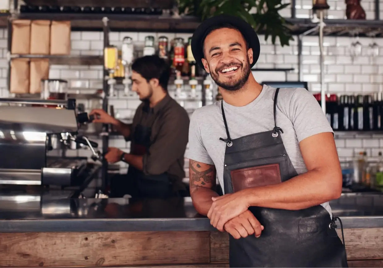 Café owner leaning on the counter while a colleague prepares coffee in the background